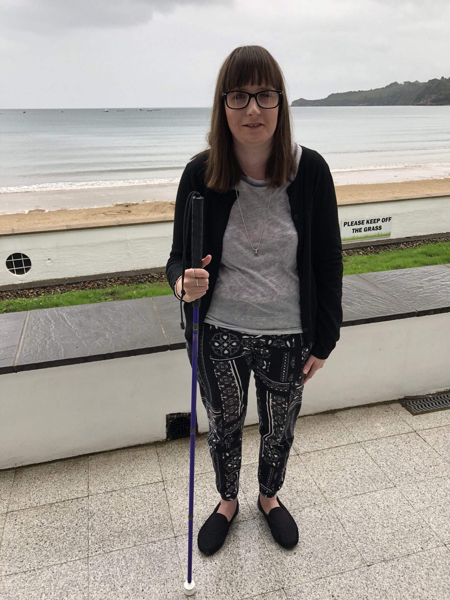 A photo of Holly holding a purple cane with the sea in the background