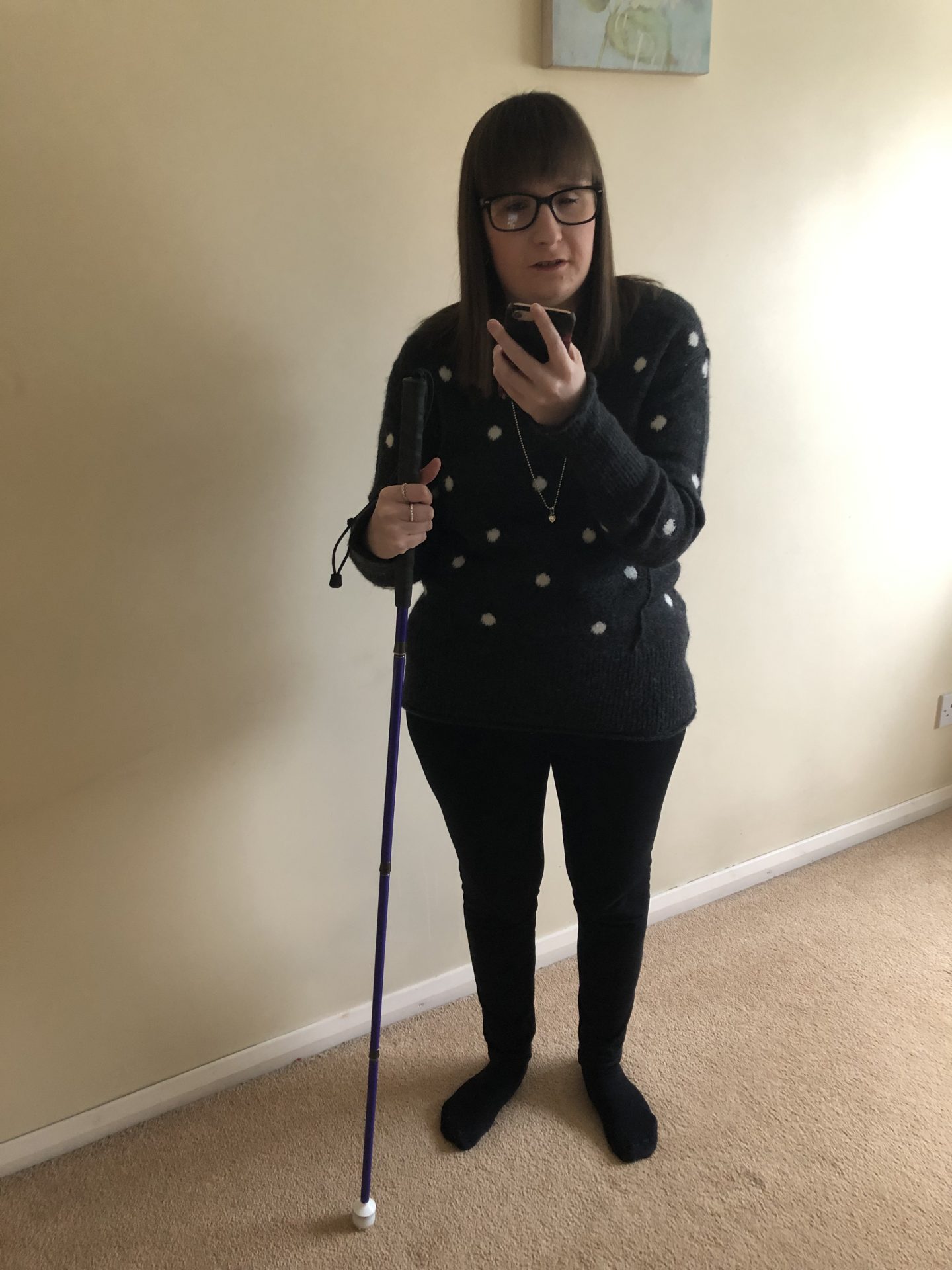 A photo of Holly holding her purple cane and looking at her phone. Her phone is in her left hand and her cane is in her right hand.