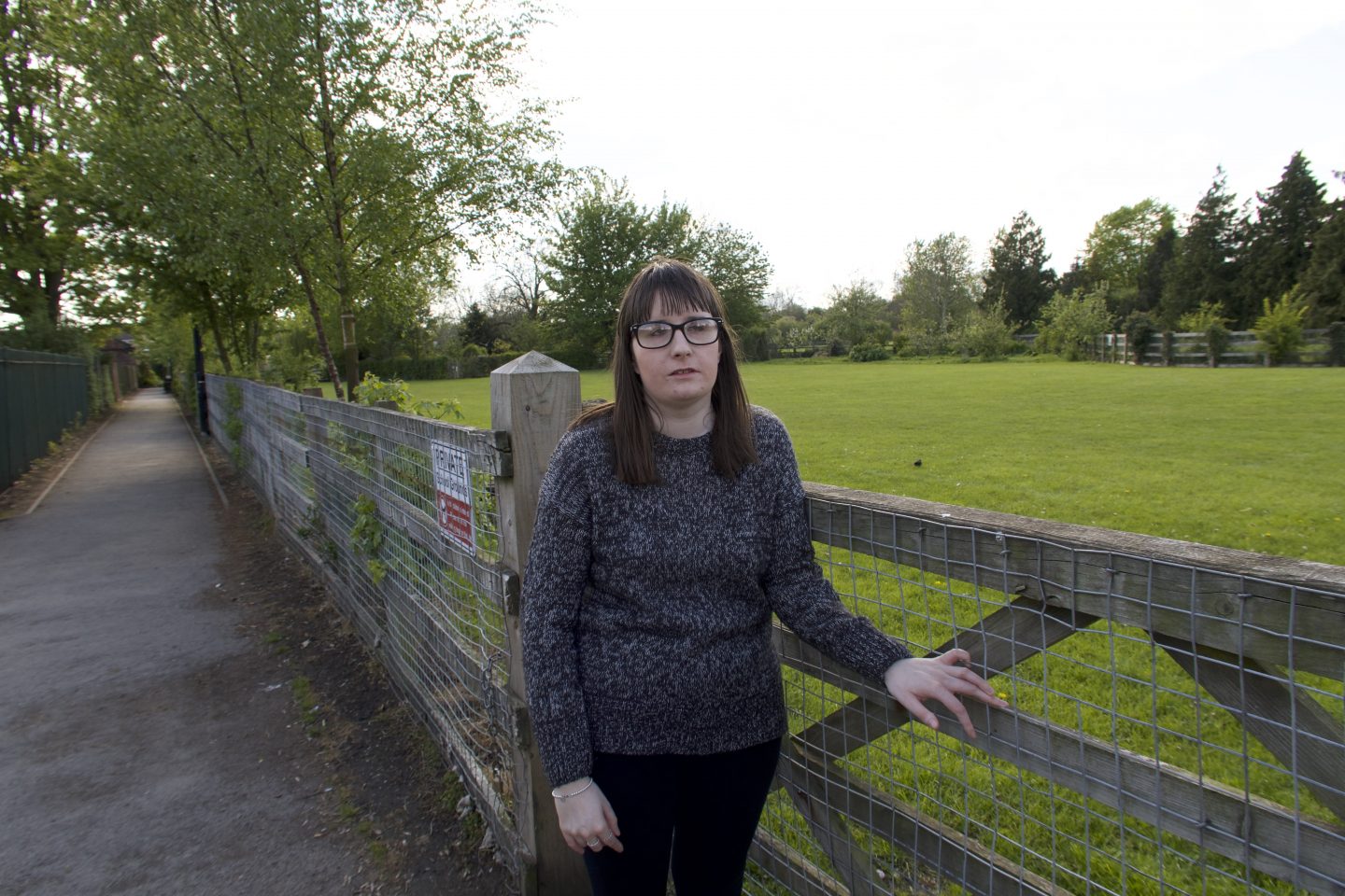 A photo of Holly with her hand on a gate, she is wearing leggings and a black jumper