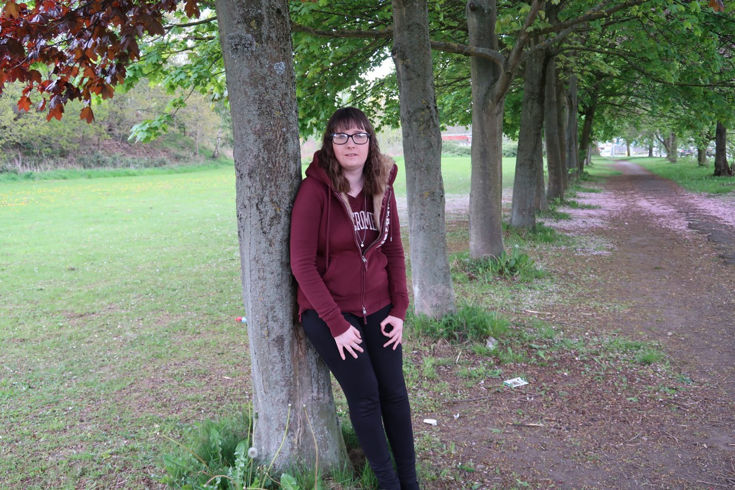 A photo of Holly stood leaning on a cherry tree in an avenue of trees