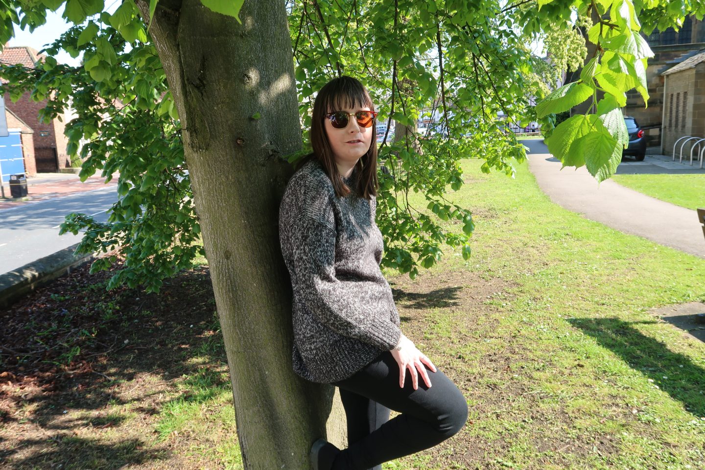 A photo of Holly leaning against a tree with her knee up on it