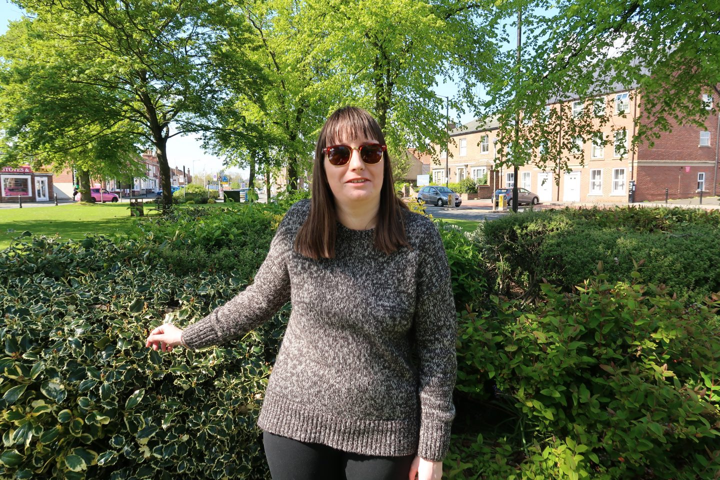 A photo of Holly stood in front of a Holly tree and pointing at it