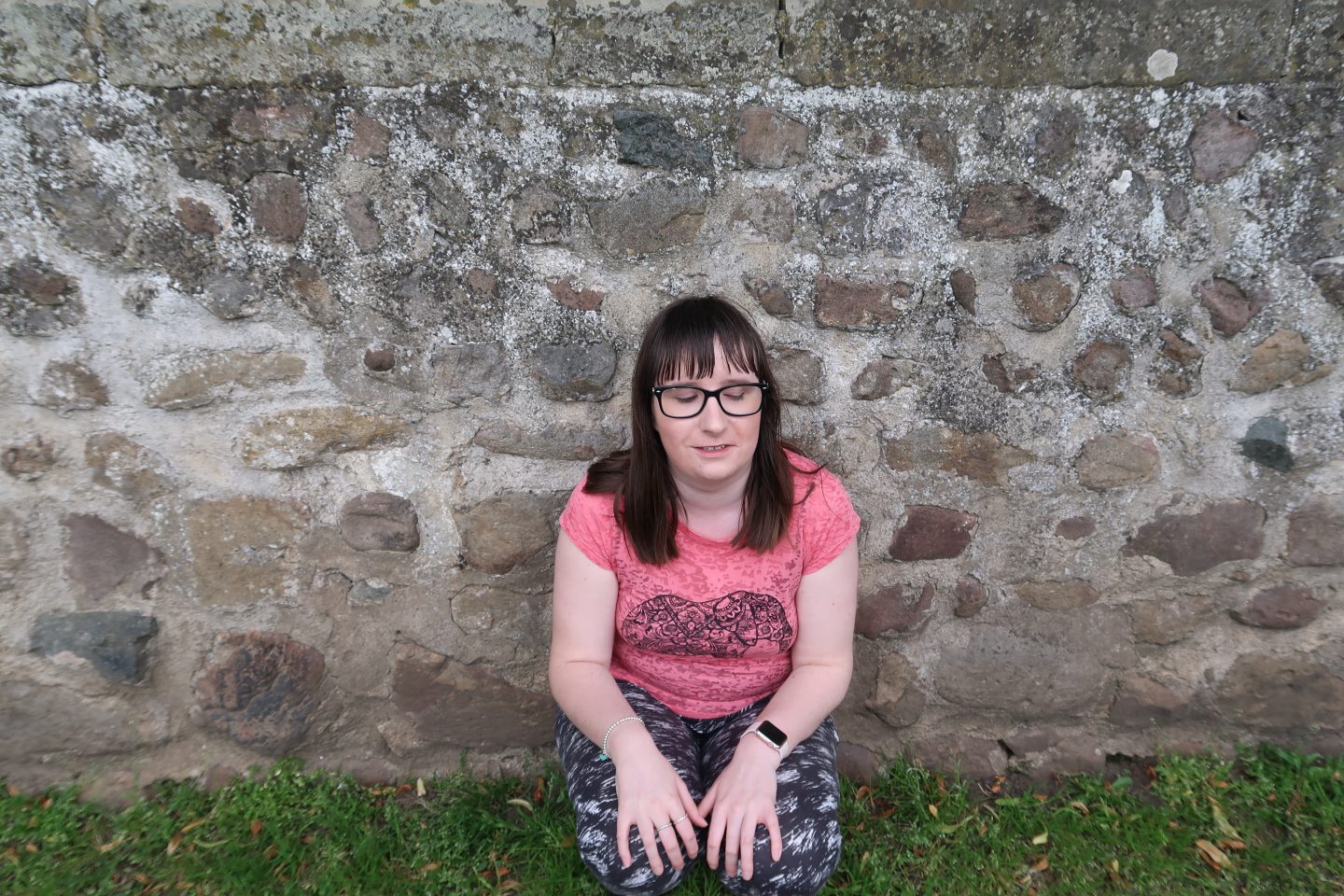 A photo of Holly knelt down in front of a stone wall