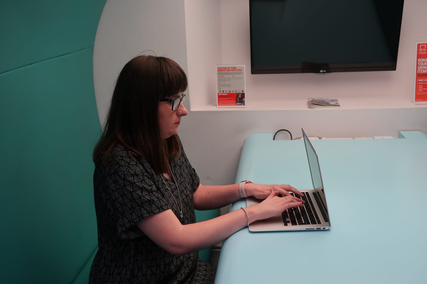 A photo of Holly sat at a desk with her laptop, she is looking away from the camera