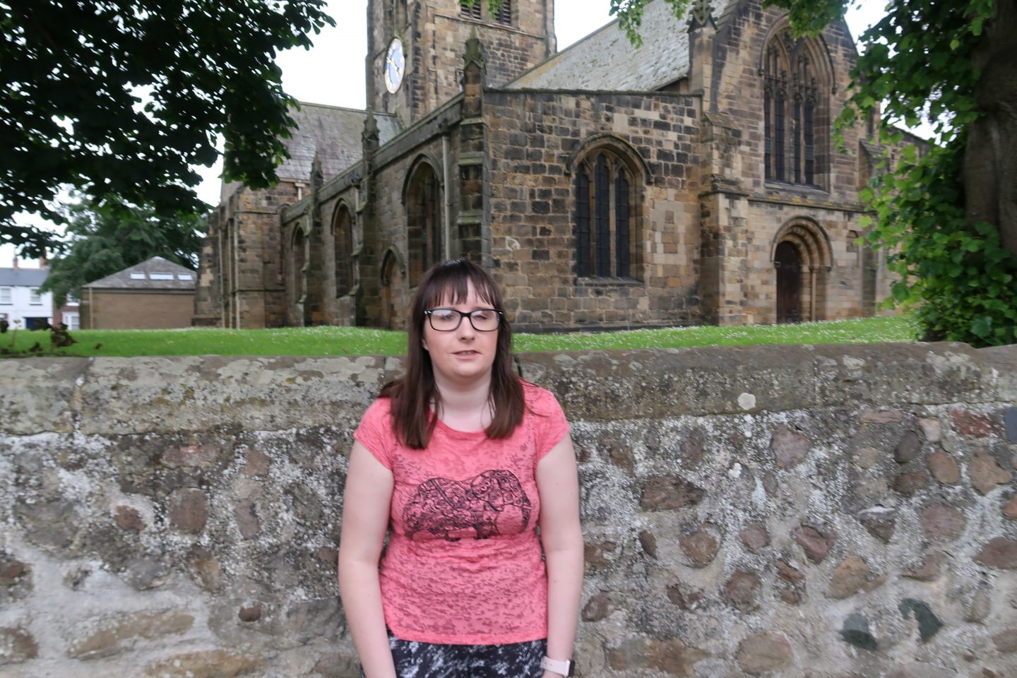 A photo of Holly stood in front of a stone wall