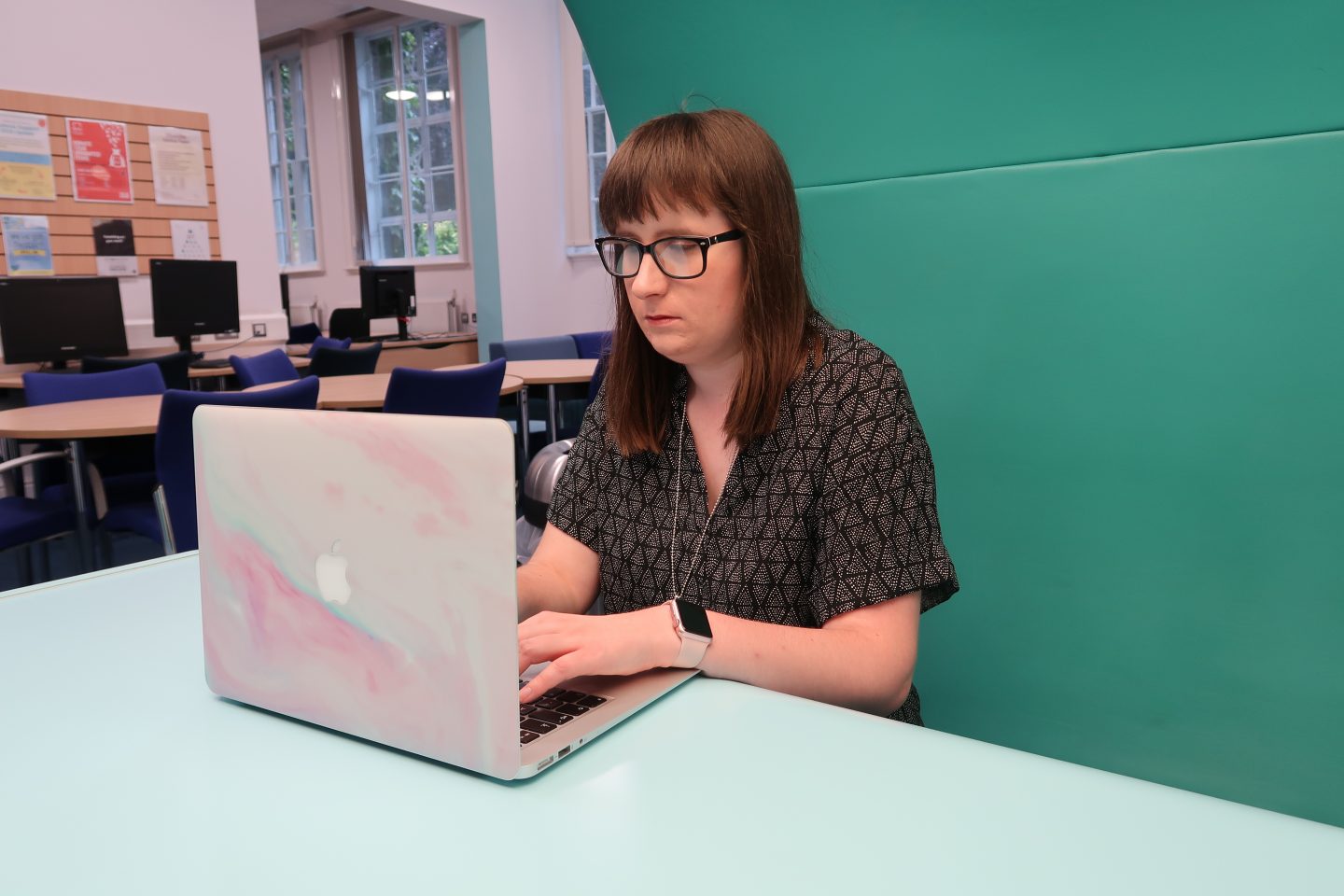 A photo of Holly sat at a desk working on her laptop, she is looking at the laptop screen