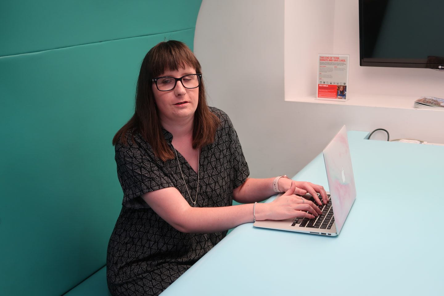 A photo of Holly sat working at a desk on her laptop, she is wearing a grey and black dress
