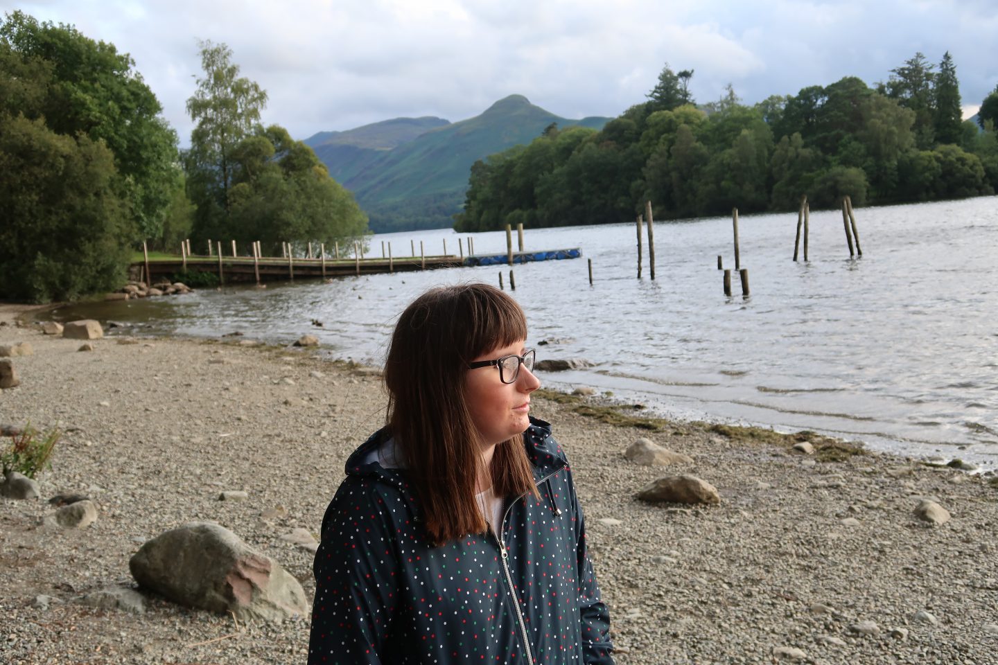A photo of Holly wearing a blue coat, there is a lake in the background