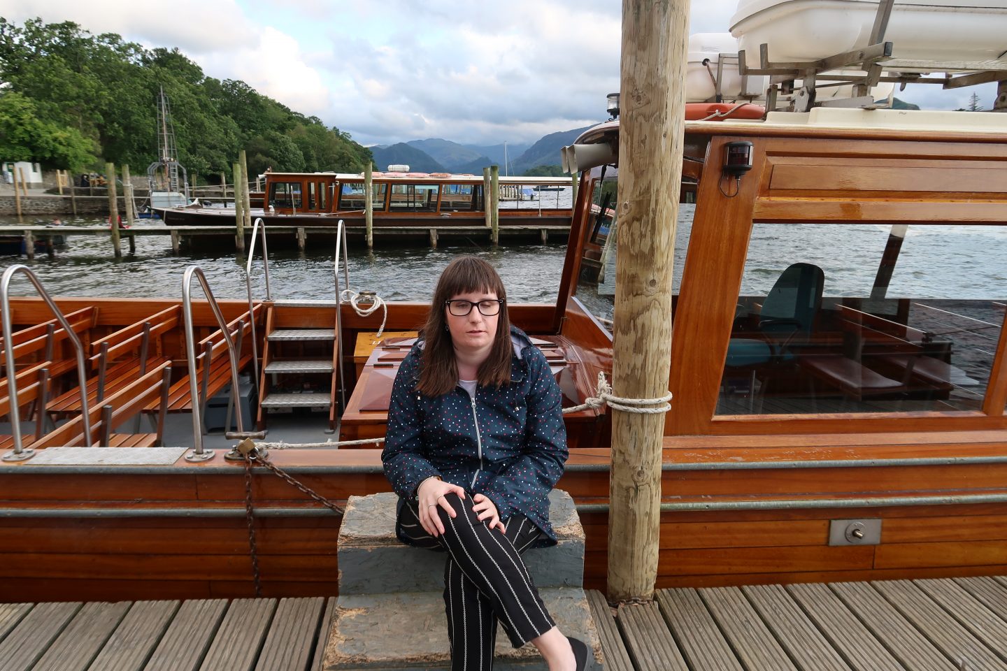 holly sat in front of a tourist boat, she is wearing a blue coat and black trousers