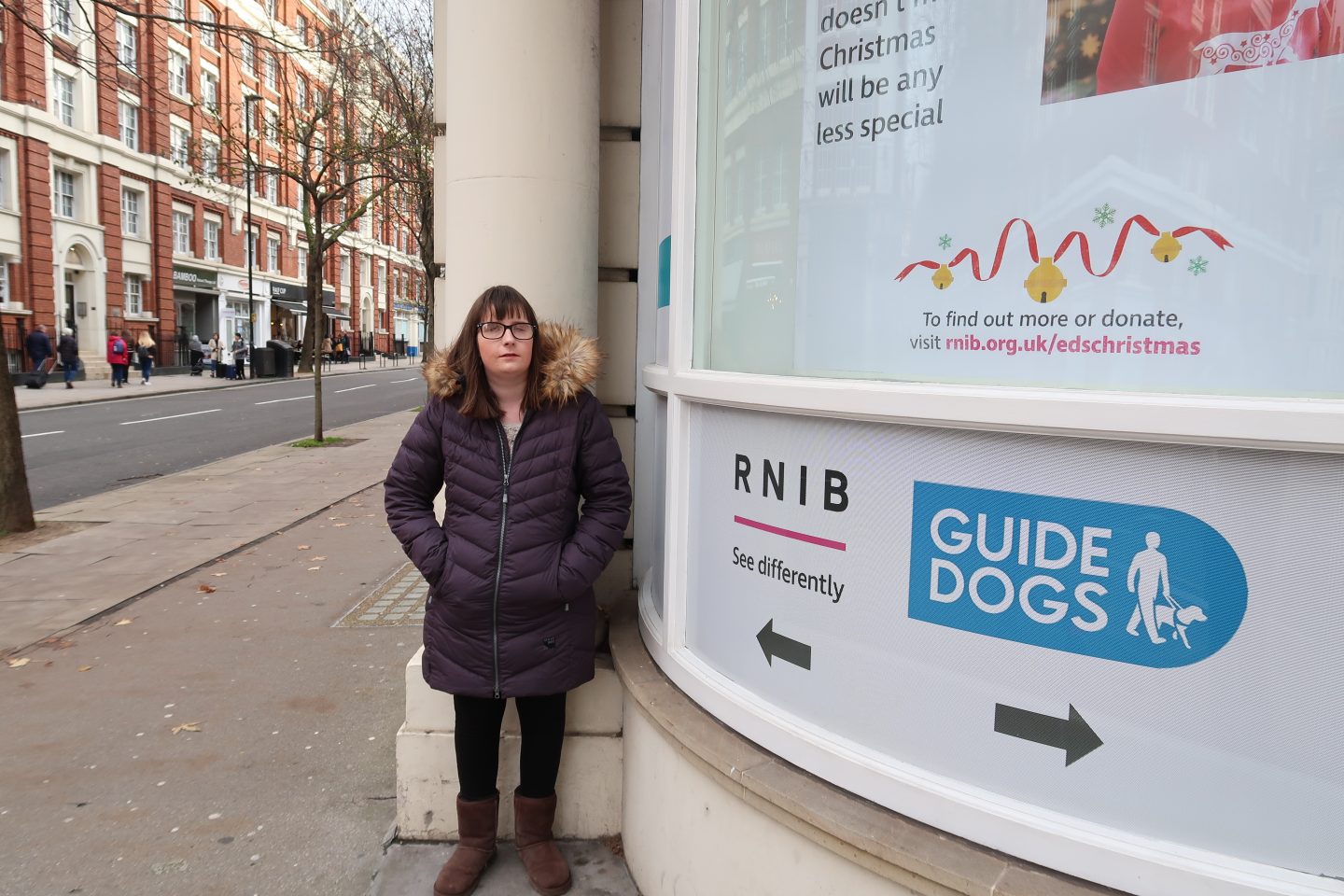 Holly stood outside the RNIB offices in London, there is a window display at the side and old victorian buildings in the background