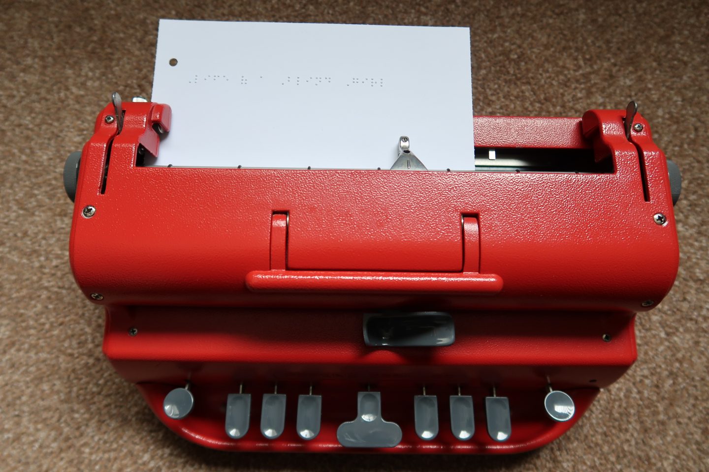 Red Perkins Brailler with paper in and braille writing that reads "Life of a Blind Girl"