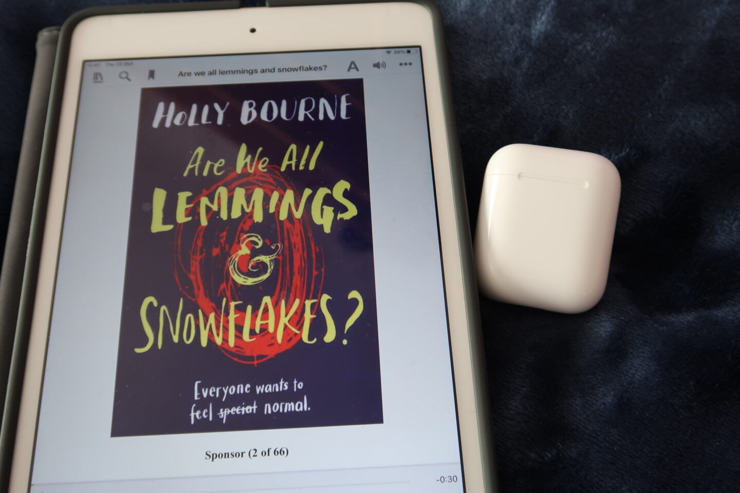 iPad which has the audiobook for Are We all Lemmings and Snowflakes by Holly Bourne on the screen, there is a pair of Apple AirPods next to it