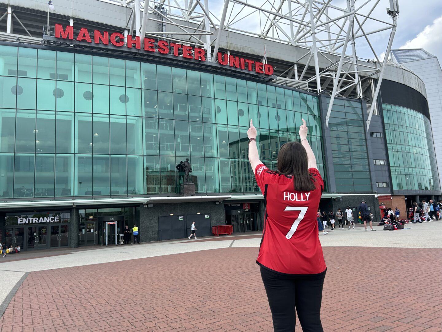 Holly stood with her back to the camera in front of the Old Trafford stadium which has the words Manchester United in bold red lettering on the front. She's wearing a Manchester United shirt that reads "Holly number 7".