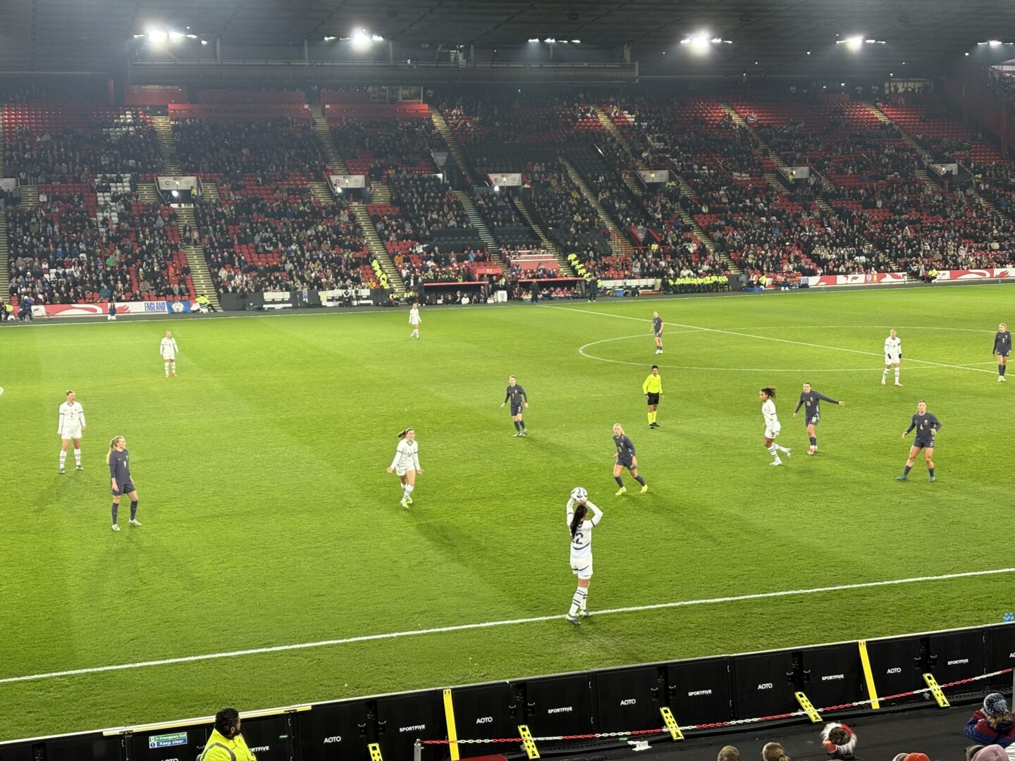 England and Switzerland players on the pitch at Bramall Lane. England are wearing their purple away kit, while Switzerland wear a white kit. A Swiss player can be seen about to take a throw-in. The stands are filled with spectators in the background.